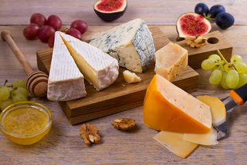 Cheese selection on wooden rustic background. Cheese platter with different cheeses, served with grapes, figs, nuts and honey. Food for wine