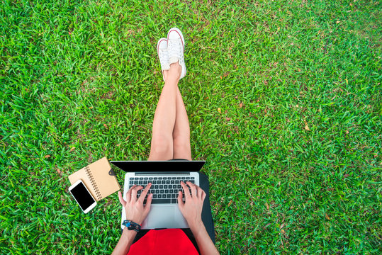 Top view of a studient woman sitting on the green grass in a park with laptop, smart phone and book. Phone with blank
