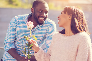 Wonderful gift. Delighted nice positive woman smiling and taking a rose while feeling happy about the gift
