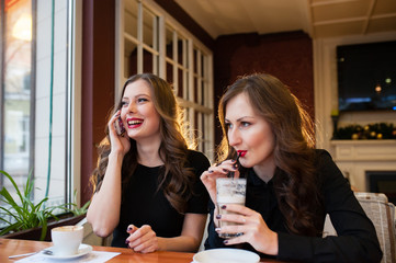 Two beautiful girls drinking coffee and talking on the phone