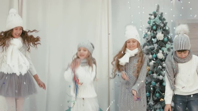 Group of merry children in sweaters and knitted caps jumping and throwing tinsel