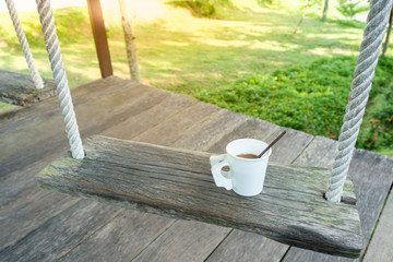 morning coffee cup on wood swing in green garden space