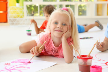 Little girl lying on floor in light room and painting