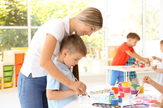 Little boy with teacher at painting lesson in classroom