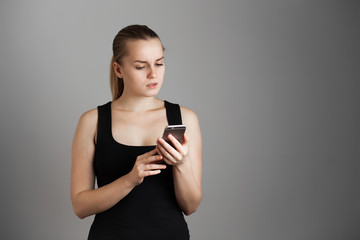 Young beautiful girl Looks at the phone and thinks, surprised. Over grey background. Copy space.