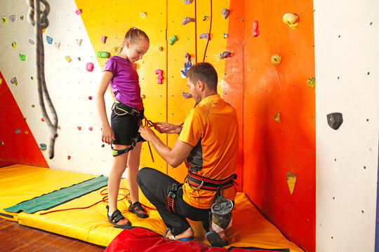 Trainer helping little girl to put on gear in climbing gym