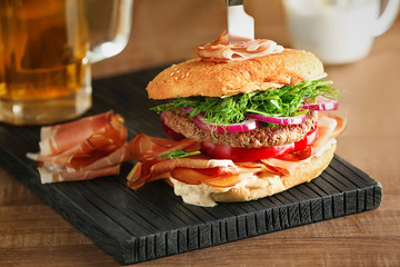 Tasty burger with prosciutto on wooden board