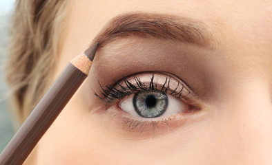 Naklejka premium Young woman correcting shape of eyebrow with pencil, close up