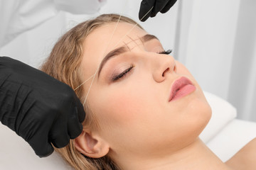 Young woman having eyebrow correction procedure in beauty salon