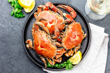 Cooked whole crabs on black plate served with white wine, black slate background, top view