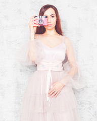 Beautiful young girl in a chic airy pink dress, takes a picture of a vintage pink camera.