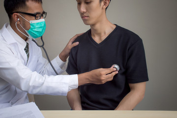 Close up doctor listening to young patient heart with a stethoscope on brown background, heart beat