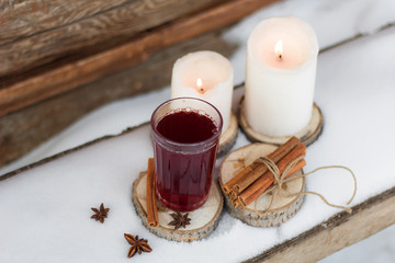 mulled wine on a wooden stand white candles bundle of dry cinnamon sticks on the table with the snow