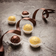 Chocolate sweets of dark and white chocolate of a round shape and a silk ribbon lie on a gray...
