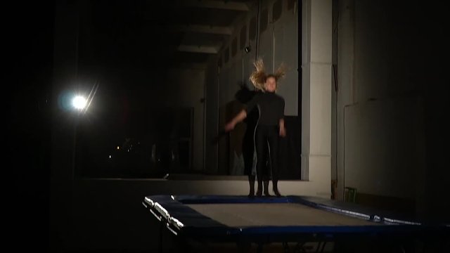 Slender long-haired woman in tights, jumping on a trampoline, slow motion