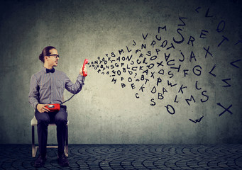 Business man holding telephone handset with alphabet letters flying out spreading news 
