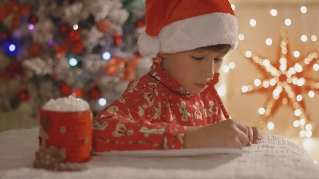 Boy in pajamas writing christmas letter to Santa Claus