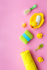 Bath accessories for kids. Yellow rubber duck, soap, sponge, brushes, towel on pink background top view copyspace