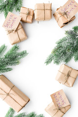 Secret Santa christmas game. Wrapped gift boxes with handwritten notes near spruce branch on white background top view copyspace