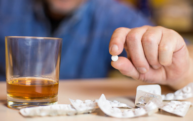 ein Mann hat eine Tablette in der Hand, ein Glas mit Alkohol und leere Tablettenpackungen liegen...