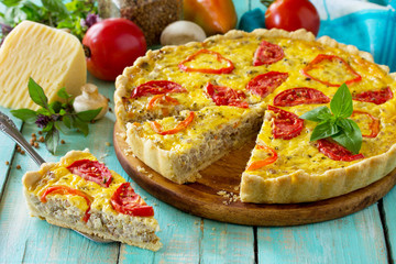 A classic quiche Lorraine pie with buckwheat, mushrooms, paprika, tomatoes, cheese and egg filling on a wooden table.