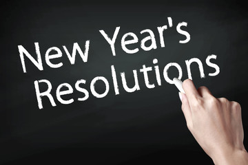 Hand holding a chalk and writing New year resolutions