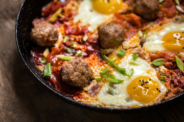 shakshuka, the Israeli dish of eggs, tomatoes and meatballs with greens on wooden background
