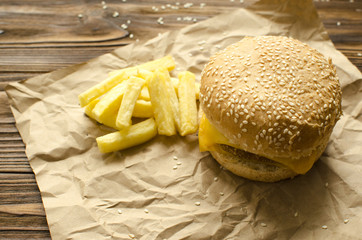 Cheeseburger with fried potatoes on a  craft paper on wooden background with space for text