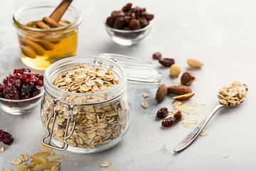 Ingredients for homemade oatmeal granola in glass jar. Oat flakes, honey, raisins and nuts. Healthy breakfast concept with copy space.