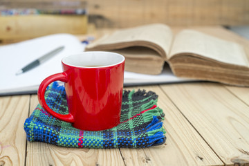Red cup of coffee and books opened diary on wooden table.
