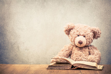 Retro Teddy Bear toy sitting at the old wooden desk with old book front concrete wall background....