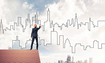Man architect draw silhouette of modern city on blue sky. Mixed 