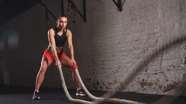 Athletic young woman doing some crossfit exercises with a rope indoor. Slow motion