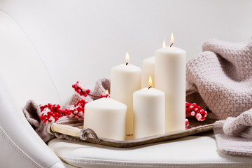 Four white burning advent candles with red berries and knitted blanket on chair
