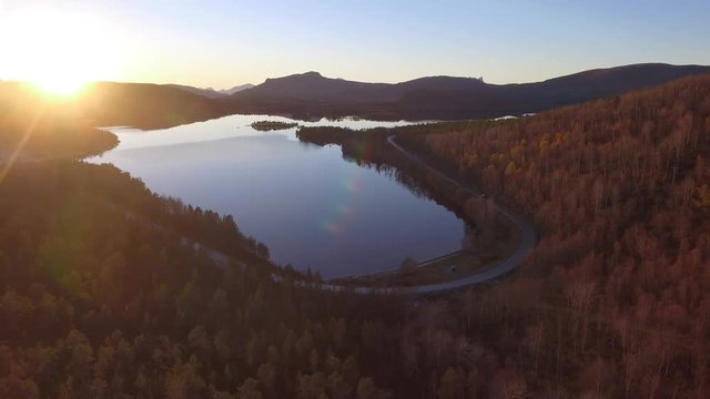Aerial Drone moving slowly backwards over beautiful orange autumn forest in Norway 4k with water lake and sunlight sunrise sunset mountains in the background 