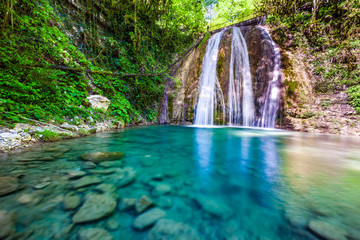 Waterfall in a green spring forest surrounded by stones, clear turquoise water on an impressive natural landscape. 33 Waterfalls, Sochi, Russia.