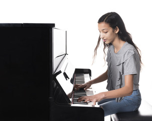 teenage brunette girl and black upright piano against white background in studio
