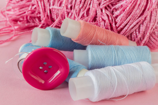 Multicolored threads, scissors, buttons, fabric and various sewing accessories on a pink background with copy space