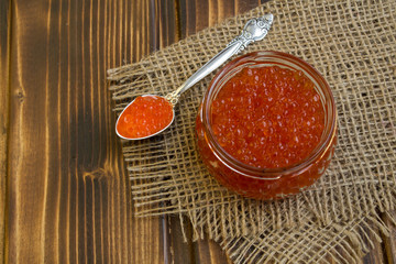 Red caviar in the glass jar on the rustic wooden background.View from above.