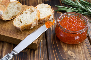 Red caviar in the glass jar and bread on the wooden background