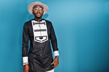 Portrait of stylish black african american man at hat and glasses against blue background.