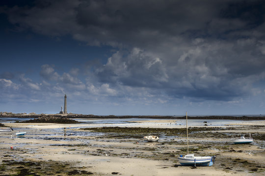 Coastline landscape in low tide with lighthouse and dried boats in Brittany, France