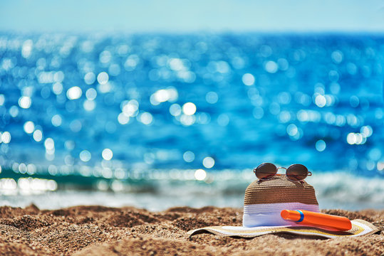 Bonnet Hat, Sunglasses And Bottle Of Sunscreen On The Beach Sand.