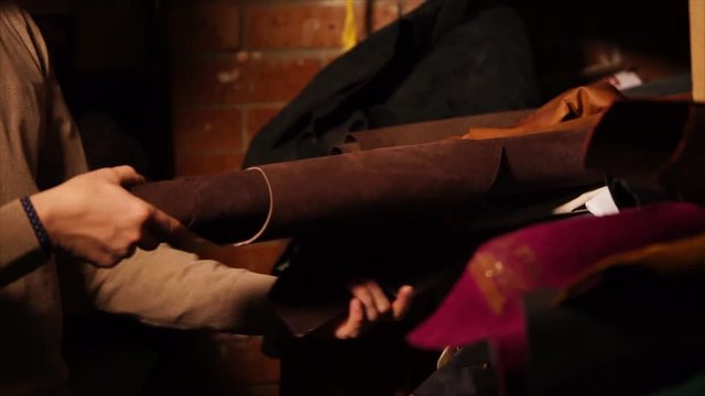close up shot of the sewing business of the master, who chooses the fabric to create the product, the man takes out a roll of suede and pulls it off the shelf, where the other fabrics lie