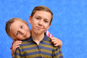 Cute couple of kids in casual clothes are giving high five, looking at camera and smiling, on gray background