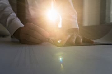 Businessman drawing with a pen and ruler at a table in a beam of bright light with sun flare