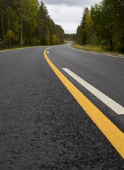 Low point of view on new asphalt road, curves ahead. White and yellow marks.