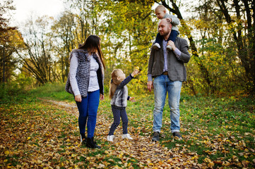 Naklejka na ściany i meble Happy caucasian family of mom dad and little girl with boy at majestic autumn fall forest.