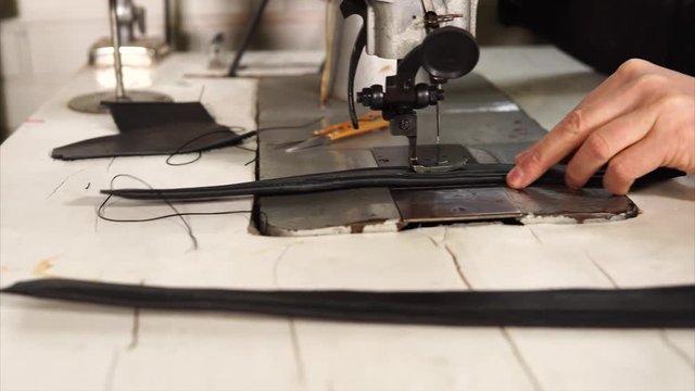 Craftsman making black leather handbag and stitching handles on sewing machine