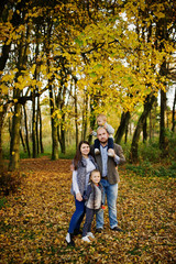 Naklejka premium Happy caucasian family of mom dad and little girl with boy at majestic autumn fall forest.